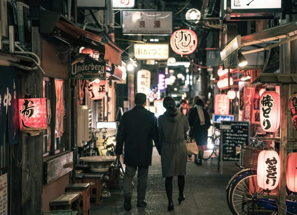 pexels-photo-1130291-1130291 Couple strolling through Osaka's bustling alley at night, surrounded by glowing lanterns and shop signs.